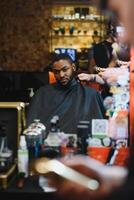 noir homme dans le salon de coiffure. mignonne noir homme fait du une la Coupe de cheveux dans le africain salon. cheveux style. la Coupe de cheveux pour adultes. photo