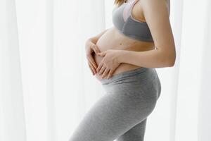 Jeune magnifique Enceinte femme permanent à Accueil près le la fenêtre. photo