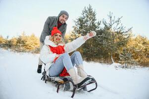 magnifique Jeune couple dans l'amour ayant amusement sur une hiver vacances dans montagnes, copain pousser petite amie sur une traîneau, profiter neigeux, brumeux hiver journée Extérieur photo