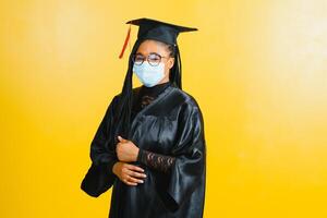portrait de une Jeune africain étudiant dans une diplômé casquette protecteur masque, sur une Jaune arrière-plan, l'obtention du diplôme 2021 photo
