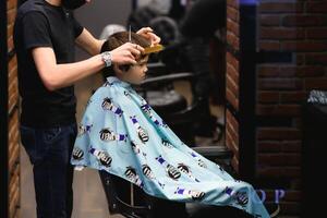 côté vue de mignonne peu garçon avoir la Coupe de cheveux par coiffeur à le salon de coiffure. photo