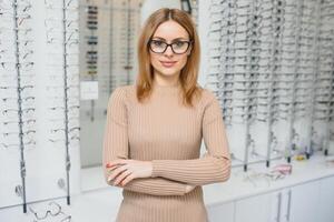 santé se soucier, vue et vision concept - content femme choisir des lunettes à optique magasin. portrait de magnifique Jeune femme en essayant Nouveau des lunettes dans opticien magasin. photo