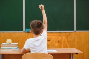 élémentaire école garçon à salle de cours bureau en essayant à trouver Nouveau des idées pour devoirs scolaires. photo