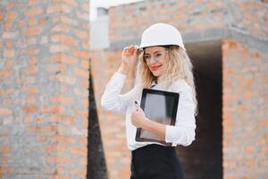 construction ingénieur. fille avec construction Documentation. une femme dans une blanc difficile chapeau contre le toit de une bâtiment. construction de une Nouveau maison photo