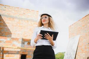 absorbé dans le travail de une femme ingénieur travail avec une tablette sur le Contexte de le construction placer. portrait de une Jeune architecte, protecteur équipement. sélectif concentrer photo