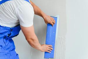 portrait de une ouvrier dans salopette et en portant une mastic couteau dans le sien mains contre le plâtré mur Contexte. réparation travail et construction concept photo