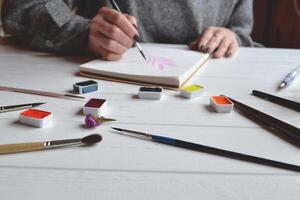 femme des peintures dans une carnet de croquis. outils pour La peinture sur le blanc en bois bureau. peintre travail. photo