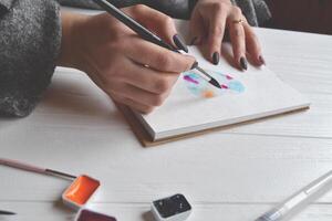 femme des peintures dans une carnet de croquis. outils pour La peinture sur le blanc en bois bureau. peintre travail. photo