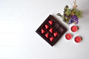 rouge des sucreries dans une forme de cœur et rouge bougies sur le blanc en bois tableau. Contexte pour salutation carte sur la Saint-Valentin journée avec endroit pour texte. photo