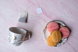 vide tasse, thé sac et soucoupe avec dessert sur une rose Contexte. photo