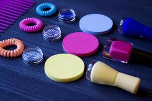 coloré et brillant produits de beauté. beauté se soucier outils. beauté salon. les filles paradis. clou polit, paillettes, rose cheveux bandes et peigne sur une foncé bleu en bois bureau. brillant encore la vie de beauté instruments. photo