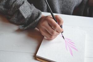 femme des peintures dans une carnet de croquis. outils pour La peinture sur le blanc en bois bureau. peintre travail. photo