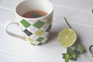 une tasse de thé, menthe branche et citron vert sur le blanc en bois tableau. photo