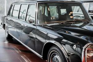 Vue avant et latérale d'une limousine de classe affaires rétro noire avec phare droit, miroir chromé et passage de roue sur sol marron