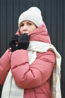 portrait de une Jeune femme dans une hiver vers le bas veste, tricoté chapeau, gants et une lumière écharpe sur une foncé Contexte. photo