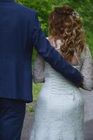 le jeune marié met le sien bras autour le de la mariée taille. la mariée dans une blanc robe avec écoulement cheveux. jeunes mariés sur une marcher. photo