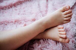 enfants jambes mensonge contre le Contexte de une rose couverture, deux jambes, pieds, franchi jambes de une enfant. photo