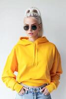 ai généré à la mode femme dans une vibrant Jaune sweat à capuche et énorme des lunettes de soleil posant à l'intérieur photo