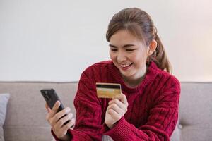 femme en portant crédit carte et en utilisant téléphone intelligent à maison, en ligne achats, en ligne bancaire, paiement, dépenses argent, commerce électronique à magasin, crédit carte concept photo