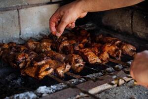 une homme main cuisiniers rôti Viande sur charbons, une prêt à l'emploi délicieux kebab, tour plus de une brochette, porc filet dans une Marinade est frit sur charbons. photo