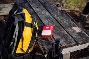 camping équipement, premier aide trousse, camping dans le forêt, Jaune sac à dos, rouge miniature premier aide trousse, blanc croix, urgence assistance à le touristique. photo