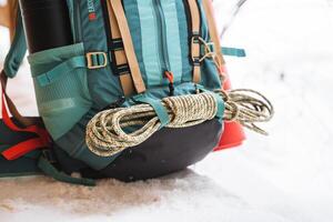 une brillant randonnée sac à dos mensonges sur le neige. une escalade corde est lié à une sac à dos. dans le côté poche de le thermos. randonnée dans l'hiver. rochers et les forêts photo