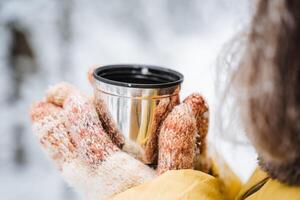 mains en portant une agresser de thé. chaud thé est versé dans une verre, boisson de une thermo agresser de café dans la nature. chaud en haut dans le hiver forêt, chaud votre mains. le concept de une tasse dans le main. photo