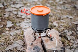 une touristique gaz brûleur sur Haut est une pot avec une couvercle, aluminium ustensiles de cuisine pour une randonnée, une lumière alliage, vaisselle supporter sur le des pierres. photo