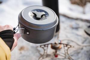 une camping poêle, une camping cuisine, soupe ustensiles, une gris pot, une main en portant une la poêle contre le toile de fond de la nature. photo