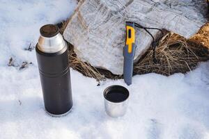 faune survie couteau, thermos avec chaud thé, boisson tasse, hiver randonnée, bushcraft dans le les bois, équipement mensonge dans le neige photo