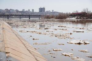 la glace sur le rivière dans le ville, pièces de la glace flotte sur le eau, printemps inondation, ville digue. photo
