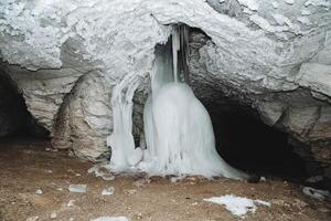 un la glace colonne les flux de le plafond de le la grotte sur le argile sol, le stalagner grandit souterrain, le stalagmite, le stalactite est congelé dans hiver, le l'eau est congelé. karst grotte. photo