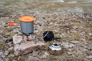 touristique ustensiles, argent bouilloire, aluminium pot avec poignées et couvercle, gaz camping brûleur, champ cuisine, cuisinier nourriture dans le forêt. photo