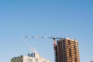 grue contre le bleu ciel. construction placer, une machine pour levage lourd charges à le la taille de une à plusieurs étages bâtiment. photo