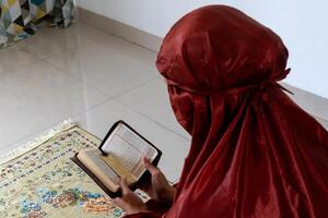 une musulman femme séance sur une prière tapis et en train de lire le coran avec indonésien Traduction photo