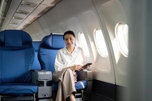 en voyageant et technologie. en volant à premier classe. Jeune affaires femme passager en utilisant téléphone intelligent tandis que séance dans avion vol photo