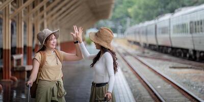 deux femmes sont content tandis que en voyageant à le train gare. tour concept. deux asiatique femmes meilleur ami Voyage haute cinq sur train calendrier dans chemin de fer station photo