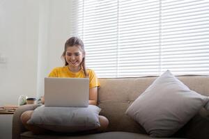 Jeune femme séance sur le canapé et travail sur projet, en train de regarder film sur portable du repos et content bavardage avec ami dans social réseau à Accueil photo