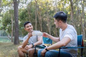 Masculin gay couple asiatique en voyageant avec tente camping Extérieur et divers aventure mode de vie randonnée actif été vacances. en buvant café et parlant ensemble photo