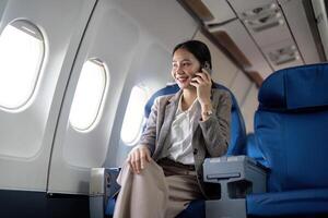 asiatique Jeune femme d'affaires réussi ou femelle entrepreneur dans formel costume dans une avion asseoir dans une affaires classe siège et les usages une téléphone intelligent pendant vol. en voyageant et affaires concept photo