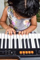 asiatique mignonne fille en jouant le synthétiseur ou piano. mignonne peu enfant apprentissage Comment à jouer piano. enfant mains sur le clavier intérieur. photo