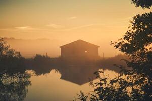 vieux Grange sur Lac rive sur brumeux lever du soleil photo