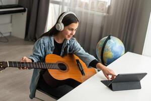 adolescent fille apprentissage à jouer guitare à Accueil en utilisant en ligne cours. loisir éloigné musical éducation acoustique guitare. copie espace photo