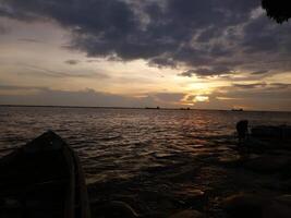 une bateau est séance sur le rive à le coucher du soleil photo