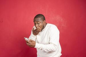 Jeune africain américain homme avec surpris faciale expression tenir téléphone intelligent dans le sien mains, dactylographie message, bavardage avec copains dans social réseaux photo