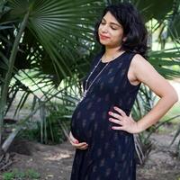 une Enceinte Indien Dame pose pour Extérieur grossesse tirer et mains sur ventre, Indien Enceinte femme met sa main sur sa estomac avec une maternité robe à société parc, Enceinte à l'extérieur maternité tirer photo