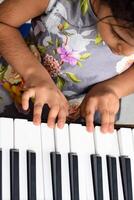 asiatique mignonne fille en jouant le synthétiseur ou piano. mignonne peu enfant apprentissage Comment à jouer piano. enfant mains sur le clavier intérieur. photo