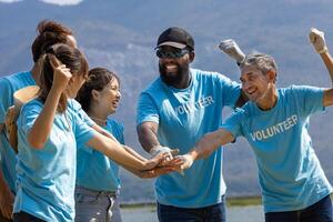 équipe de Jeune et la diversité bénévole ouvrier groupe prendre plaisir charitable social travail Extérieur ensemble à économie environnement projet portant bleu T-shirt tandis que joindre main dans Puissance assembler unité photo