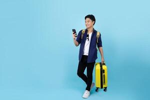 content Beau asiatique touristique homme en portant téléphone intelligent avec en portant valise sac Aller à Voyage sur vacances isolé sur bleu Contexte. photo