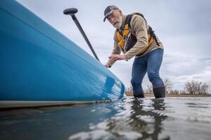 Sénior Masculin pagayer une supporter en haut planche à pagaie sur une Lac dans de bonne heure printemps, grenouille la perspective de un action caméra à l'eau niveau photo